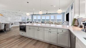 A modern kitchen with a large island, white cabinetry, and pendant lighting. - Bluebell: Beachfront, Private Pool, Arcade Games, Plantation (St. George Island)