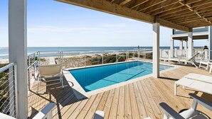A wooden deck with a pool, white lounge chairs, and a view of the beach and ocean. - Bluebell: Beachfront, Private Pool, Arcade Games, Plantation (St. George Island)