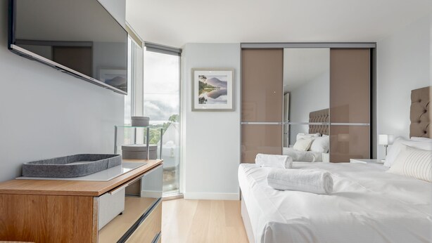 A modern bedroom with a bed, bedside tables, a large window, and a sliding door. - Westburn Lane Apartments (No 2) (St Andrews)