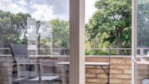 A balcony with chairs and a table, a brick wall, and a view of trees and sky. - Westburn Lane Apartments (No 2) (St Andrews)