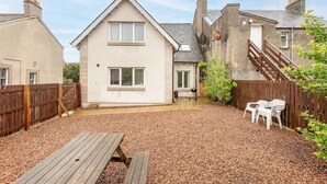 A two-story house with a gravel patio, wooden fence, and a wooden bench. - Kinnessburn Villa (St Andrews)