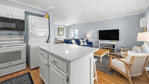A compact kitchen with modern appliances, a central island, and a cozy seating area with a TV and lamp. - Ocean Block 2 BR Unit Ready for Summer Fun! (Ocean City)