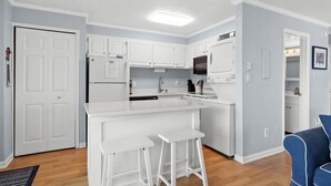 A modern kitchen with white cabinets, a central island with stools, a microwave, and a dishwasher. - Ocean Block 2 BR Unit Ready for Summer Fun! (Ocean City)