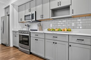 A modern kitchen with grey cabinetry, a stainless steel refrigerator, an oven, a microwave, and a fruit display on the counter.