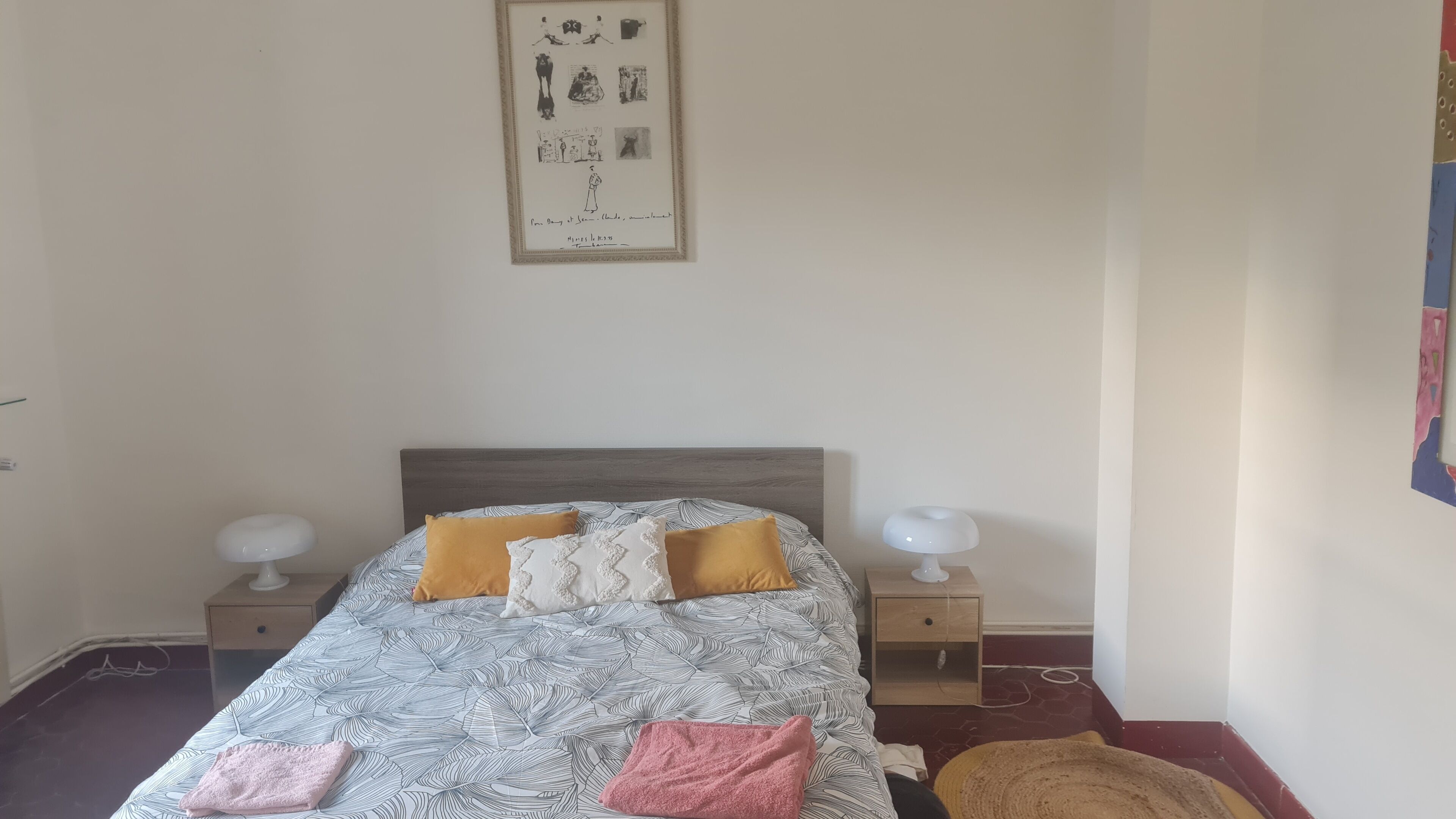 Una cama bien tendida con ropa de cama estampada y varias almohadas, flanqueada por mesitas de noche con lámparas.