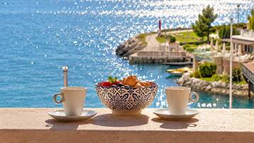 Vista sul mare da un balcone, con una ciotola di frutta e due tazze.