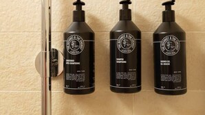 Drei schwarze Flaschen mit Produkten von The Botanist & The Chemist auf einer gefliesten Wand.