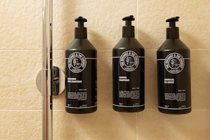 Trois bouteilles noires des produits de la marque The Botanist & The Chemist sont posées sur un mur carrelé.