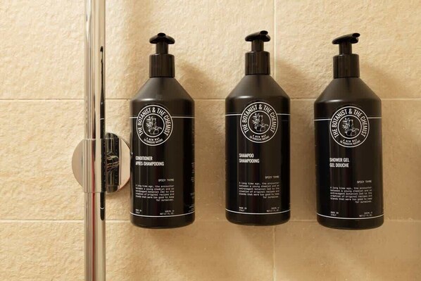 Drei schwarze Flaschen mit Produkten von The Botanist & The Chemist auf einer gefliesten Wand.