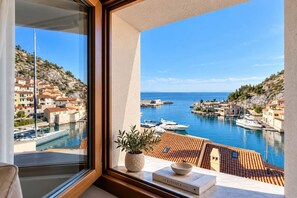 Une vue depuis un balcon donnant sur une marina, avec des bateaux, un ciel dégagé et une colline parsemée de bâtiments.