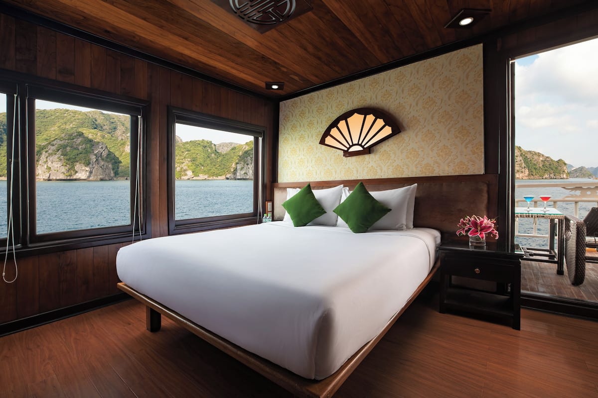 A bedroom with a large bed, wooden walls, a decorative fan, and a view of the sea.