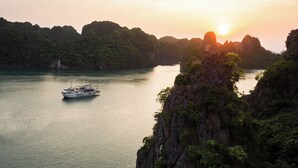 A boat on a calm river surrounded by lush green hills. - Garden Bay Classic  (Bai Chay)