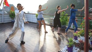 A group of people practicing Tai Chi on a wooden deck with potted plants and a railing. - Garden Bay Classic  (Bai Chay)