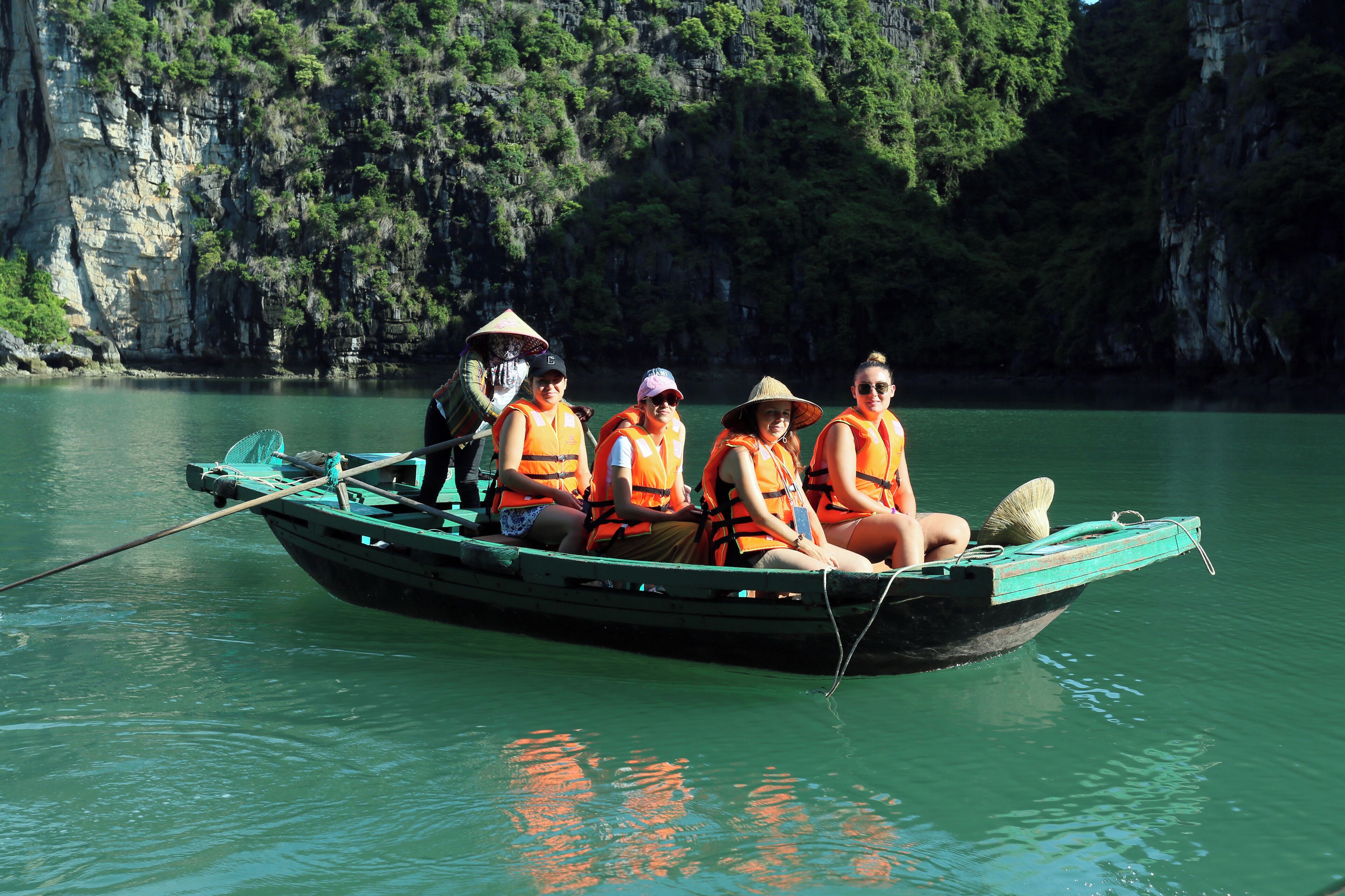 A group of people in a boat on a calm river with rocky cliffs in the background.