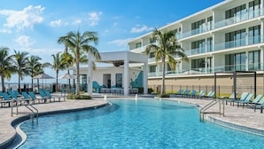 A swimming pool with lounge chairs and palm trees, surrounded by a modern building with balconies.
