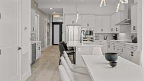 A modern kitchen with white cabinetry, a central island, and a dining area with white chairs.