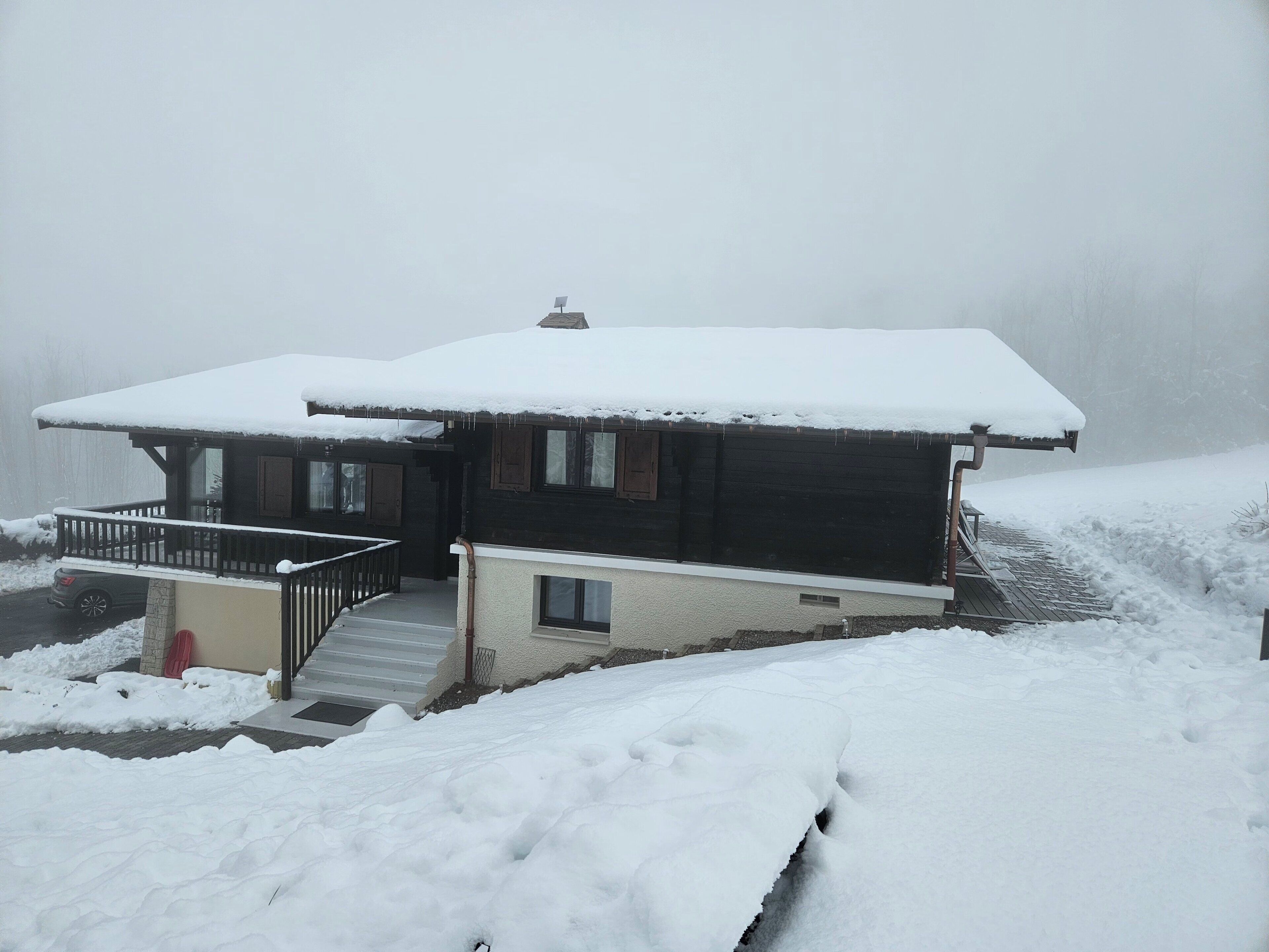 A two-story wooden house with a snow-covered roof and a small porch.
