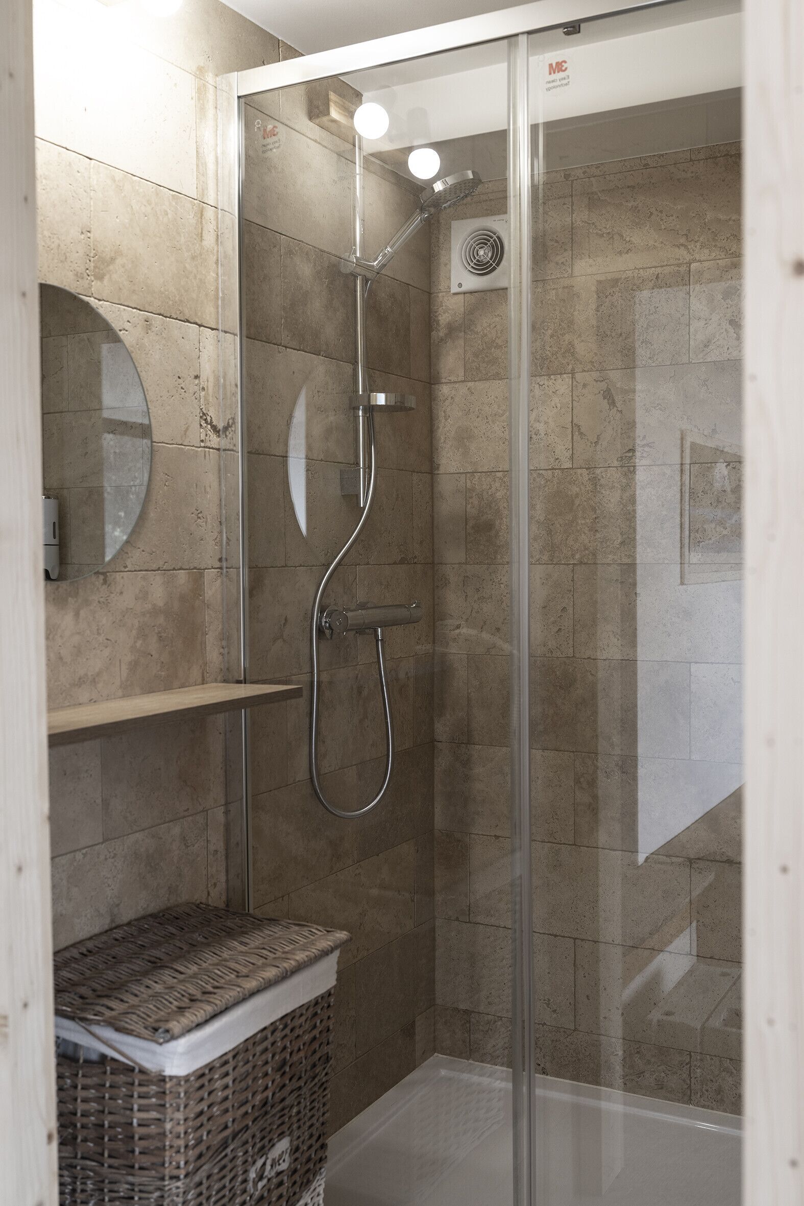 A glass-enclosed shower with a handheld showerhead and a wall-mounted control panel.