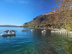 A calm lake with boats, clear water, and a hillside with trees and houses.