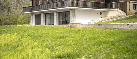A two-story chalet with a balcony, stone foundation, and a view of a mountainous landscape.
