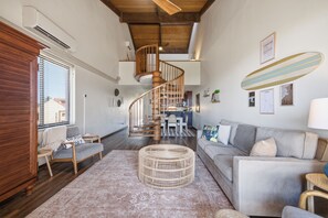 A spacious living room with a wooden staircase, a grey sofa, and a dining area.