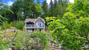 A two-story house with a balcony, surrounded by a stone wall and greenery.