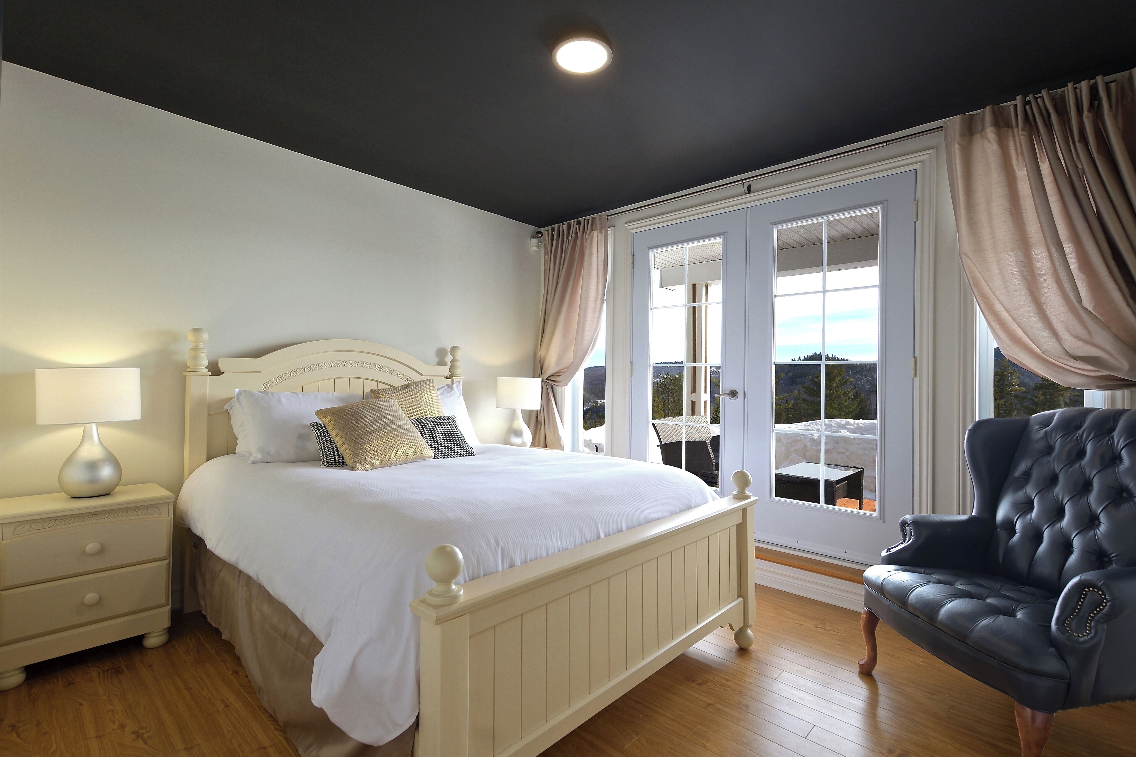 A bedroom with a bed, nightstand, lamp, and a view of the outdoors through a window.