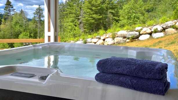 A hot tub with a wooden deck and a view of a forested hillside.