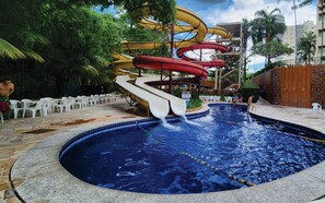 Una piscina con varias toboganes de agua, rodeada de palmeras y un muro de piedra.