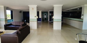 A hotel lobby with a reception desk, a sofa, and a tiled floor. - Golden Dolphin Express - HotFérias (Caldas Novas)