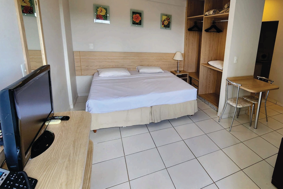 A hotel room with a bed, a desk with a computer, a chair, a small table, and a wardrobe.