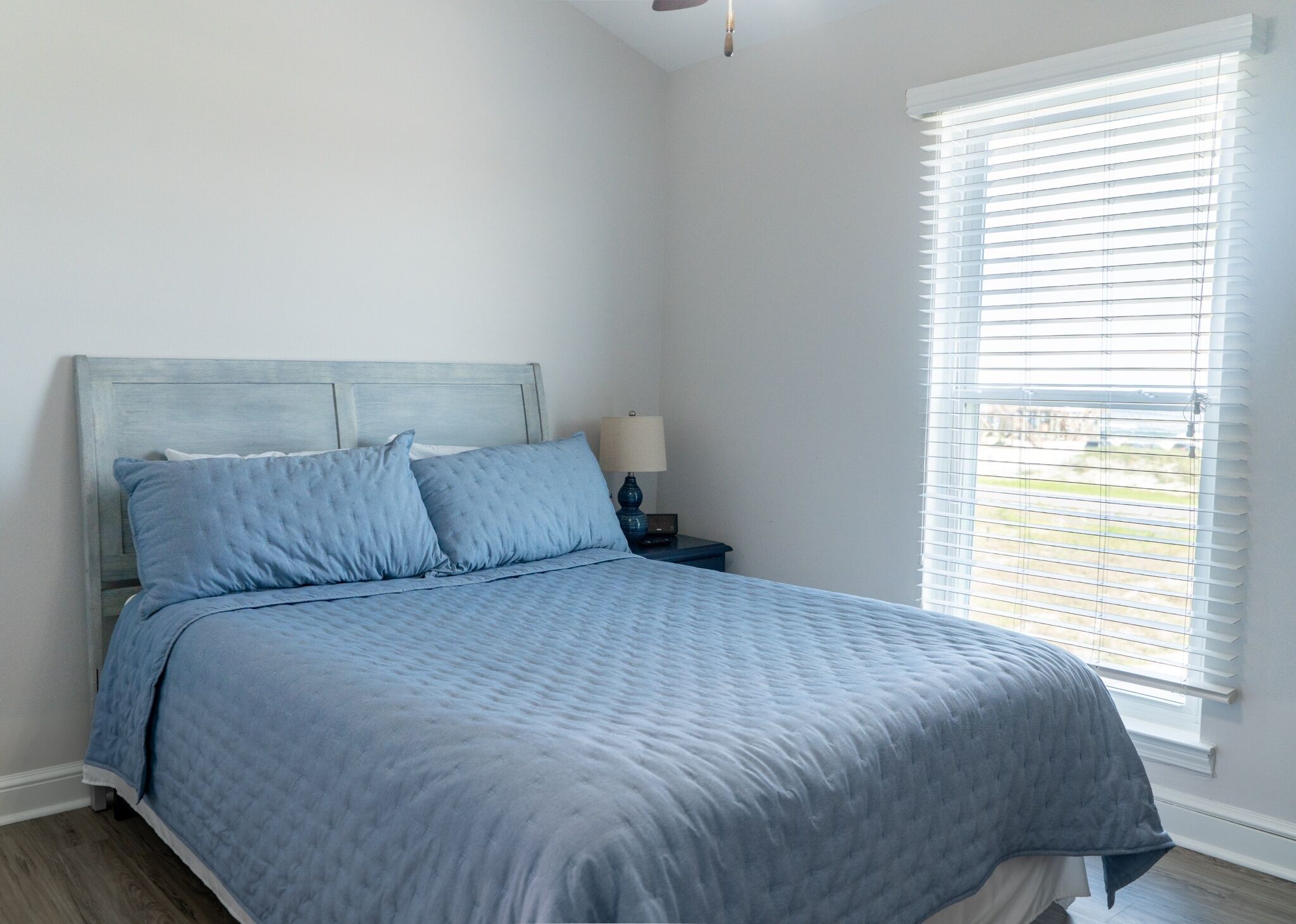 A bedroom with a bed, a nightstand, a lamp, and a window with blinds.