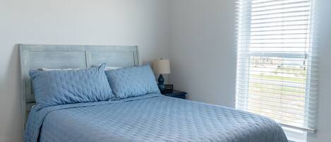 A bedroom with a bed, a nightstand, a lamp, and a window with blinds.