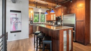 A modern kitchen with wooden cabinets, stainless steel appliances, and a bar area with stools. - Blackhawk 2817 4 Bedroom Townhouse by RedAwning (Steamboat Springs)