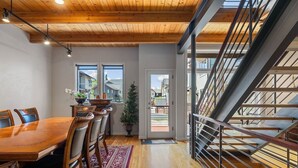 A modern dining area with a wooden table and chairs, a red rug, and a staircase with metal railings. - Blackhawk 2817 4 Bedroom Townhouse by RedAwning (Steamboat Springs)
