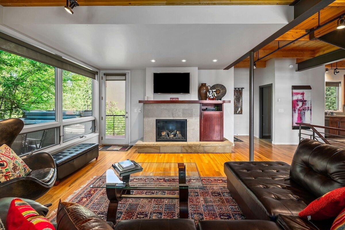 A modern living room with a fireplace, leather sofas, and a large window overlooking greenery.