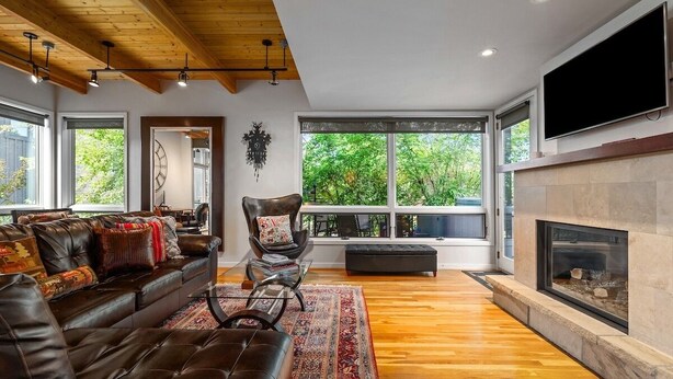 A modern living room with a leather sofa, a fireplace, and large windows offering a view of greenery. - Blackhawk 2817 4 Bedroom Townhouse by RedAwning (Steamboat Springs)