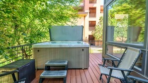 A wooden deck with a hot tub, lounge chairs, and a view of a building with balconies. - Blackhawk 2817 4 Bedroom Townhouse by RedAwning (Steamboat Springs)