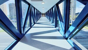 Une passerelle piétonne couverte, dotée de panneaux de verre et de poutres métalliques, qui mène à l’entrée d’un bâtiment.