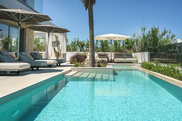 A pool area with lounge chairs, umbrellas, and a hammock.