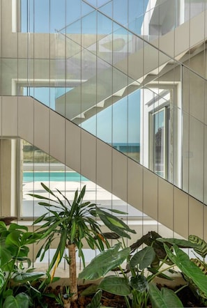 A modern interior with a glass staircase, indoor plants, and a view of a pool.