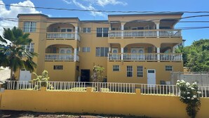 A multi-story yellow building with balconies, a white fence, and a palm tree. - Scott Beach Villa #5 (St. Thomas)