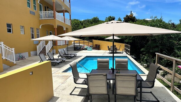 A poolside area with lounge chairs, umbrellas, and a pool. - Scott Beach Villa #5 (St. Thomas)