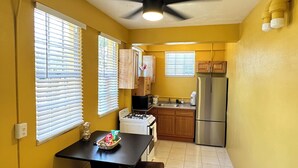 A compact kitchen with yellow walls, a stove, a refrigerator, and wooden cabinets. - Scott Beach Villa #5 (St. Thomas)
