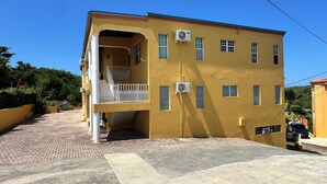A yellow building with multiple windows, a balcony, and air conditioning units. - Scott Beach Villa #5 (St. Thomas)