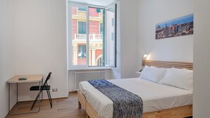 Ein Schlafzimmer mit Bett, Schreibtisch und Fenster mit Blick auf die Stadt.