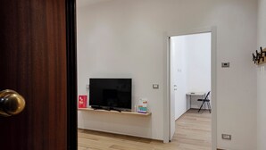 Ein modernes Wohnzimmer mit einem Flachbildfernseher auf einer Holzkonsole, einem kleinen Tisch mit Stuhl und einer Tür zu einem anderen Raum.