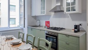 Eine moderne Küche mit Gasherd, Spüle und integriertem Backofen. Es gibt grüne Schränke und ein Fenster, das für natürliches Licht sorgt.