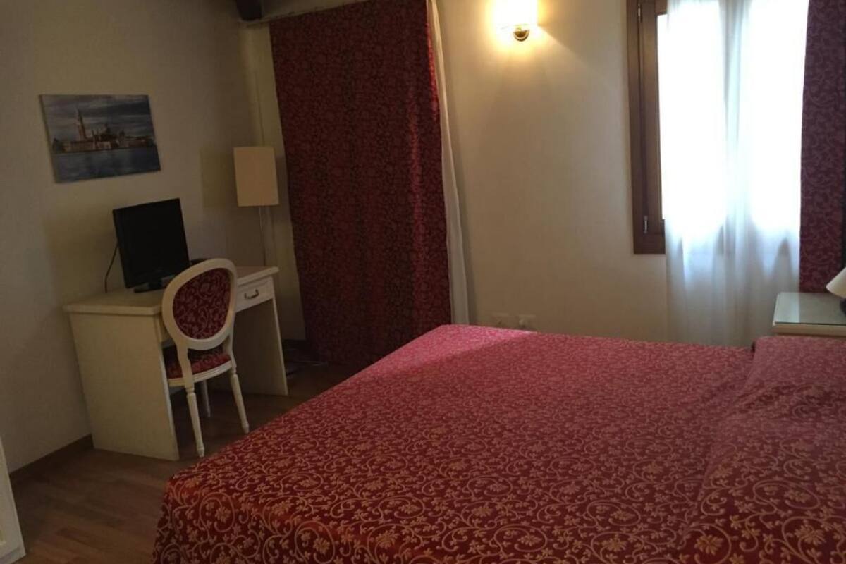 Una camera da letto con un letto, una scrivania, una sedia, una lampada e una finestra con tende.