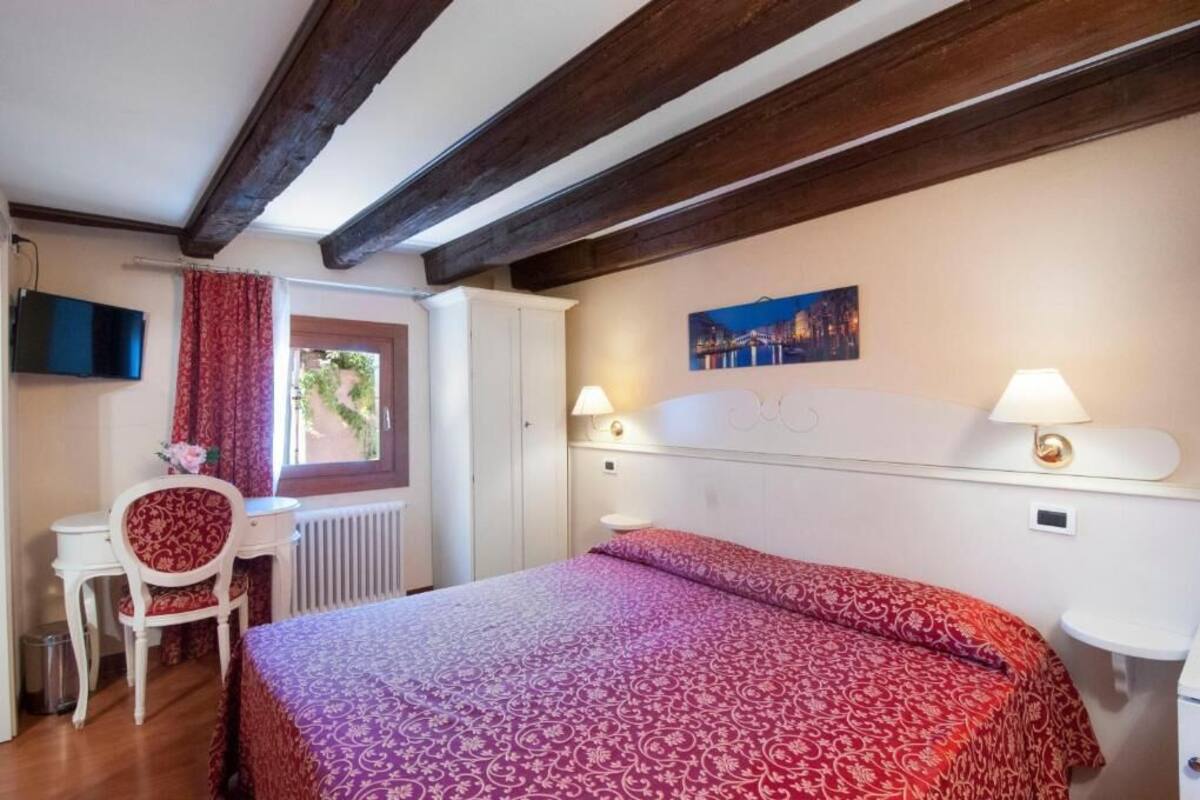 Una camera da letto con un letto, una scrivania, una sedia, una finestra e un quadro appeso al muro.